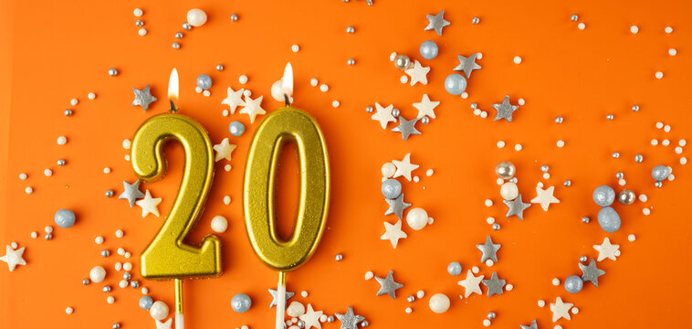 Birthday or anniversary celebration concept. Candles in the shape of the number twenty on an orange background among decorative ornaments. 20th anniversary. Banner