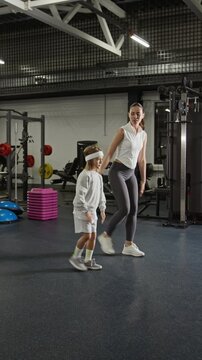 Vertical video of Caucasian young adult woman training Caucasian child in gym, performing lunges together. Footage is perfect for family fitness and healthy lifestyle campaigns
