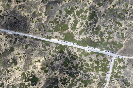 Aerial view of a road winding through a natural landscape with parked cars scattered along the roadside in Portugal.