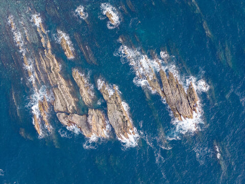 Aerial view of jagged rock formations rising from the deep blue sea with crashing waves along the coastline of Portugal.