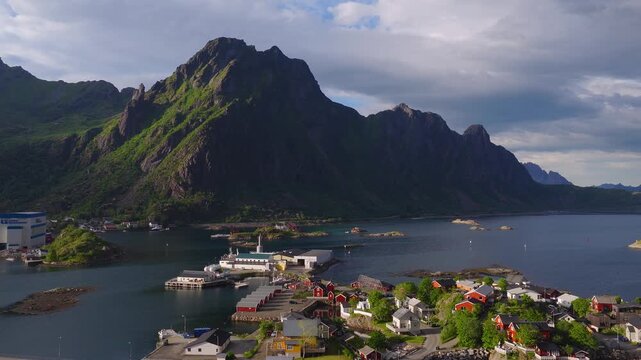 Aerial view of coastal settlement houses, harbor piers, and steep rocky mountain peaks surrounded by sea water in Svolvaer, Lofoten, Norway.
