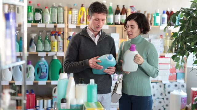 Couple adult man and woman buyers choosing laundry detergent in household chemicals store