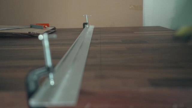 Metal guide rail clamped along a walnut countertop with a utility knife visible in the background