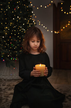 6-Year-Old Girl Blowing Out Candle Under Christmas Tree in evening near gurlands and wish moment. New year celebrating vertical