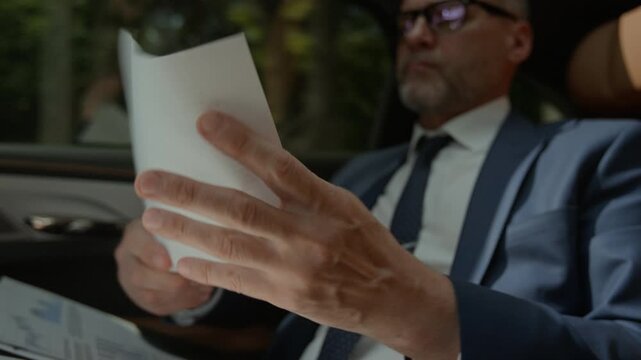 Middle aged Caucasian businessman reading documents in back seat of moving car, getting frustrated and crumpling paper. Footage represents financial crisis, business failure or executive stress