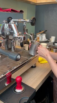 Coffee preparation, latte art making, and cafe culture. A barista frothing milk in a stainless steel pitcher using a professional espresso machine
