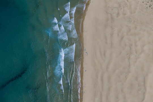 Aerial view of the sandy coastline and turquoise ocean waves crashing on the shore in Portugal.
