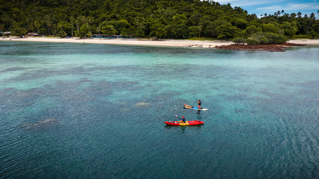 Top aerial view of Group of tourist are enjoy on water sport paddle sup-board with kayaking along at the edge of the sea beach under crystal clear of water in the island of summer trip