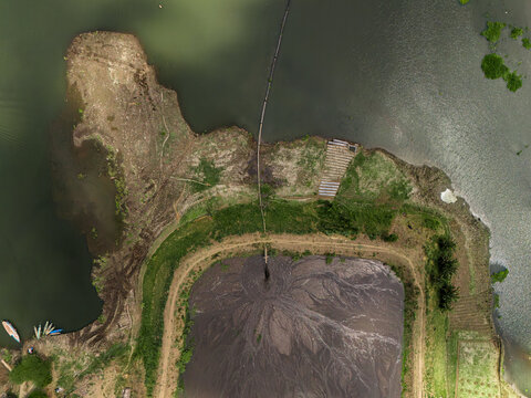 Aerial view of the Sengguruh Dam showing a long floating discharge pipeline system channeling pumped sludge slurry across the water toward the shore in Malang, East Java, Indonesia.