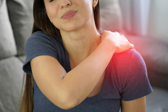 Young woman suffering from acute shoulder pain, holding painful arm with periarthritis concept