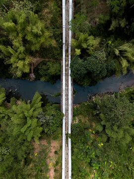 Aerial view of the Talangagung Metro Syphon with two large parallel pipes crossing over a river surrounded by lush tropical vegetation and bamboo trees in Malang, East Java, Indonesia.