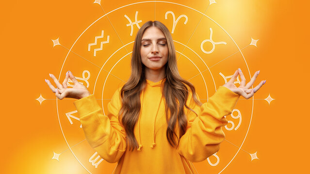 Woman in orange hoodie relaxes with zodiac signs in background