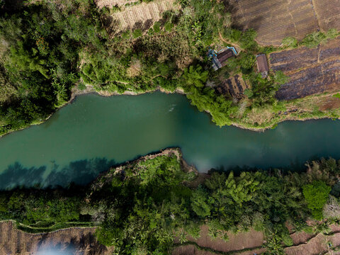 Aerial view of the Brantas River flowing through the PLTA Sengguruh hydroelectric facility, surrounded by lush vegetation and agricultural fields in Malang, East Java, Indonesia.