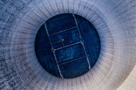 Aerial view of the interior of the decommissioned Kraftwerk Heyden cooling tower in Lahde, showing textured concrete walls and dark grid structures in Petershagen, Germany.