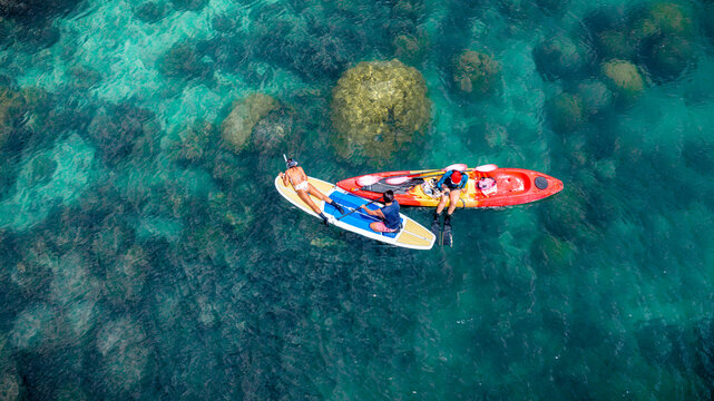 Top aerial view of Group of tourist are enjoy on water sport paddle sup-board with kayaking along at the edge of the sea beach under crystal clear of water in the island of summer trip