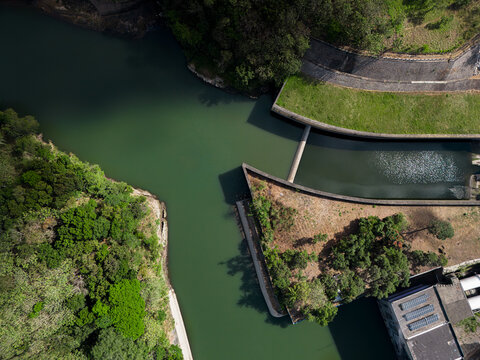 Aerial view of PLTA Sengguruh hydroelectric power plant with its water intake structure, lush green vegetation, and river flow in Malang, East Java, Indonesia.