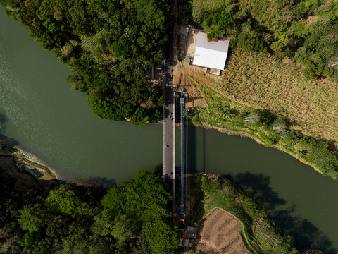 Aerial view of Sengguruh Bridge spanning the river, surrounded by lush tropical trees and nearby structures in Malang, East Java, Indonesia.