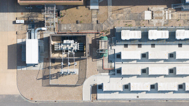 Aerial view of Brigg Renewable Energy Plant showing industrial infrastructure, electrical transformers, and rows of white storage containers on a concrete pad in Scawby, England, United Kingdom.