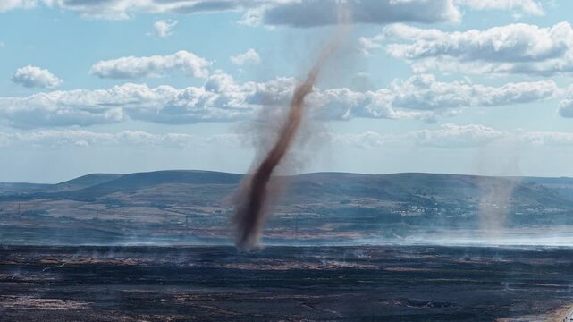 Smoke whirl spinning over burnt moorland on Llangynidr Moors, Brecon Beacons, charred earth and distant Welsh valleys under broken summer clouds