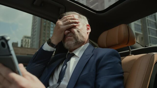 Middle aged Caucasian businessman sitting in back seat of moving car, holding tablet, taking off glasses and rubbing face and eyes. Ideal for corporate wellness and mental health campaigns