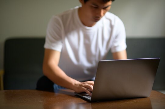 Young Man Working on Laptop at Home in Casual White T-Shirt