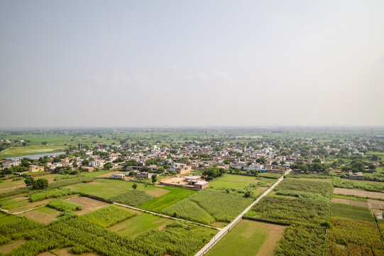 Aerial view of the NTPC Thermal Power Plant in the distance overlooking a rural settlement surrounded by lush green agricultural fields in Dadri, Uttar Pradesh, India.