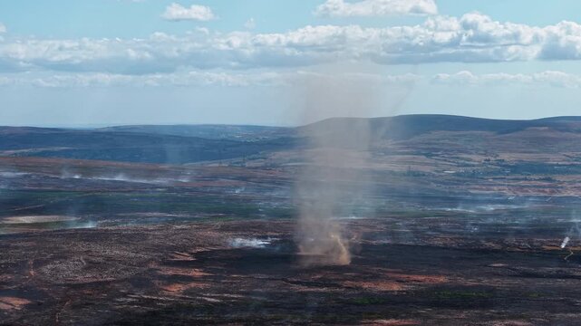 Smoke whirl and ash devil forming over scorched moorland after a wildfire, charred heathland smoldering under cumulus clouds on Llangynidr Moors in Wales