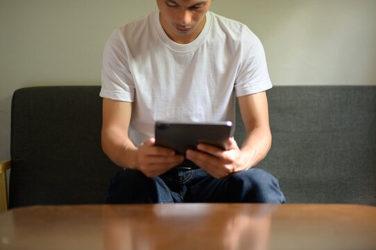 Man in White T-Shirt Using Tablet While Sitting on Couch
