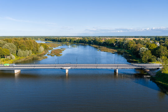 An aerial view shows a vehicle driving across a modern highway bridge spanning the calm waters of the Salaca river in Salacgriva, Latvia.