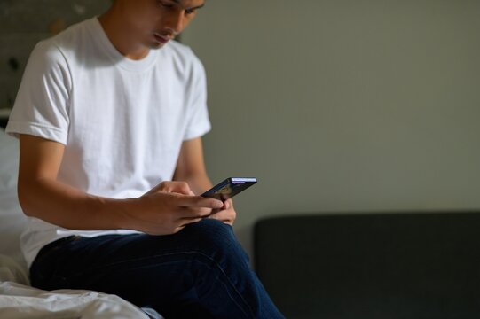 Young Man Using Smartphone While Sitting on Bed in Casual Setting