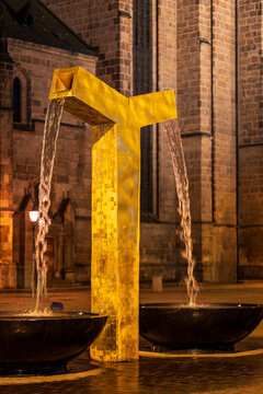 Modern golden fountain Chrtice illuminated at night with the historic St Bartholomew Cathedral in the background in Pilsen Czech Republic.