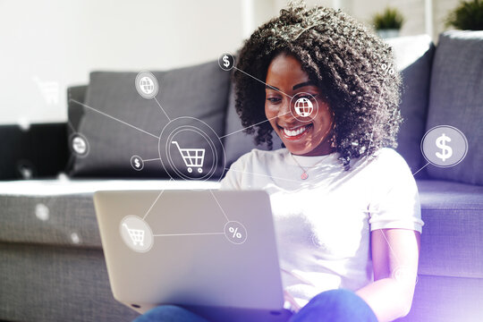 Smiling woman sits on sofa using laptop for online shopping in living room during the day