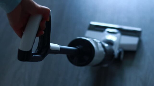 A person holds a vacuum cleaner while cleaning the floor in a room. The sunlight enters through a window and highlights the floor. The task seems important for maintaining cleanliness.