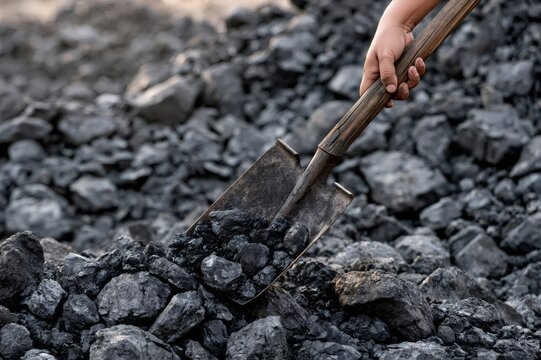Hand holding shovel digging coal for energy production
