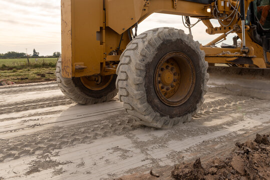 Close-up of motor grader wheel and moldboard blade grading a dirt road on a construction site