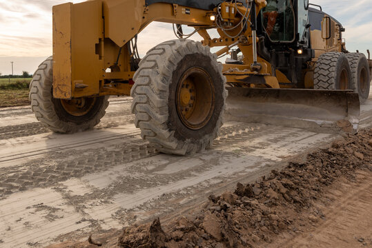 Close-up of motor grader wheel and moldboard blade grading a dirt road on a construction site
