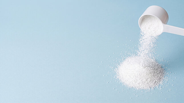 White protein powder pouring from a measuring scoop onto a blue background.
