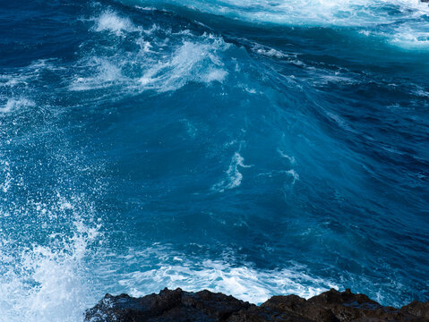 Blue ocean waves breaking over dark coastal rocks