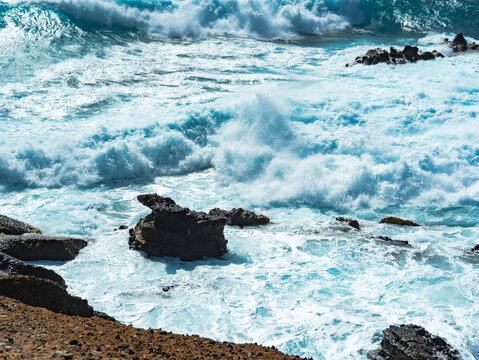 Turquoise waves breaking over dark coastal rocks
