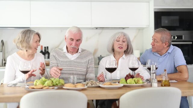 At the table, happy group of adults enjoy their holiday, drink red wine and talk together
