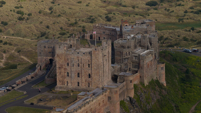 Aerial view of Bamburgh Castle with its historic stone walls and towers surrounded by grassy dunes in Bamburgh, England, United Kingdom.