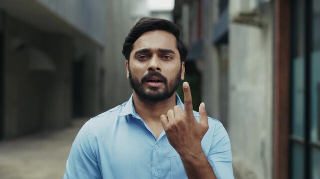 Portrait of young Indian businessman talks using sign language outdoors slow motion. Deaf bearded male gestures expressing feelings in urban block. Non verbal communication