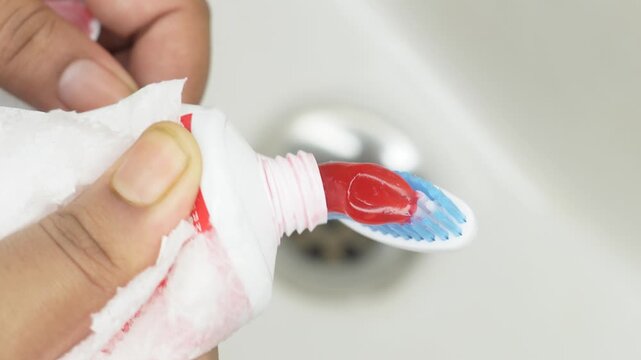 Close up hand holding applying toothpaste to toothbrush, isolated on sink background. brushing teeth daily in morning and evening. Dental health care and hygiene concept.