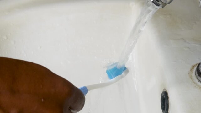 Close-up of woman washing her toothbrush under running water. woman holding brush and cleaning rubbing with fingers under the tap water in the basin.