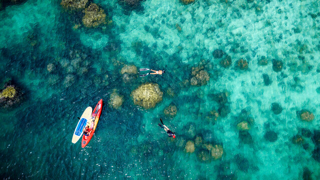 Top aerial view of Group of tourist are enjoy on water sport paddle sup-board with kayaking along at the edge of the sea beach under crystal clear of water in the island of summer trip