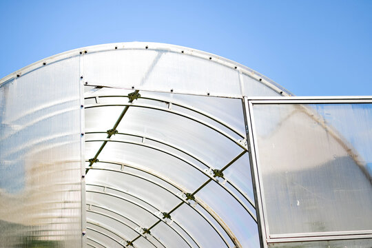 Modern arched greenhouse with transparent panels and metal frame against a clear blue sky