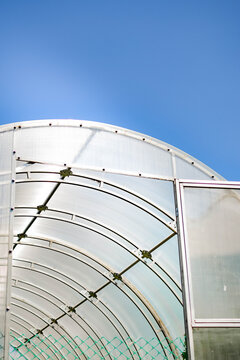 Modern arched greenhouse with transparent panels and metal frame against a blue summer sky