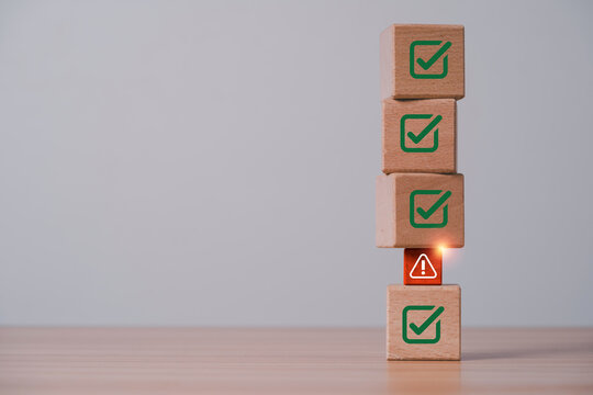Risk management concept with warning symbol interrupting green check marks on stacked wooden blocks for compliance issues, quality control, audit, assessment and business problem detection.