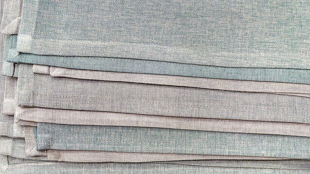 Stacked linen fabric textiles showcasing varying textures and subtle blue and gray tones, creating a layered pattern for backgrounds and material concepts