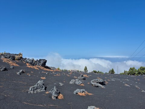 Volcanic rocks scattered on black lapilli field above clouds at Tajogaite volcano